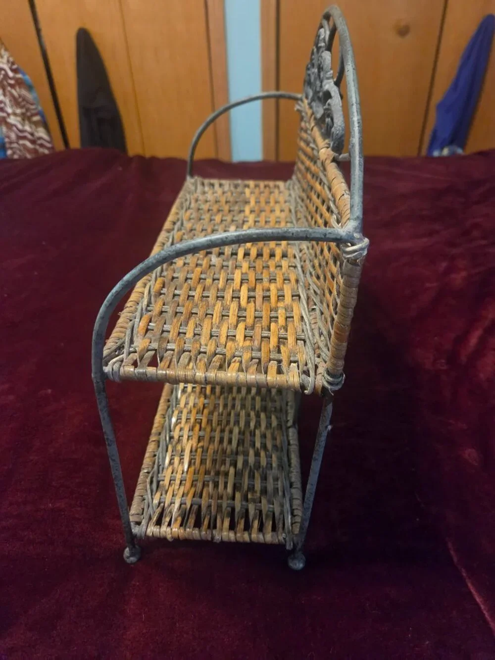 two tier wicker shelf with metal frame adorned with scrollwork some wear